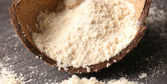 Une photographie de farine de coco d'un blanc crémeux, présenté dans une noix de coco