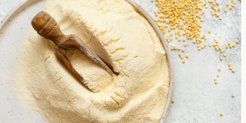 Une photo représentant de la farine de millet dorée disposée sur une surface claire, accompagnée de grains millet éparpillés. Cette image illustre la texture fine et la couleur caractéristique de la farine de millet, mettant en valeur son aspect naturel et son origine céréalière. Cela permet de décrire visuellement le sujet principal de l'article tout en restant fidèle à son contenu sur la farine de millet sans gluten.